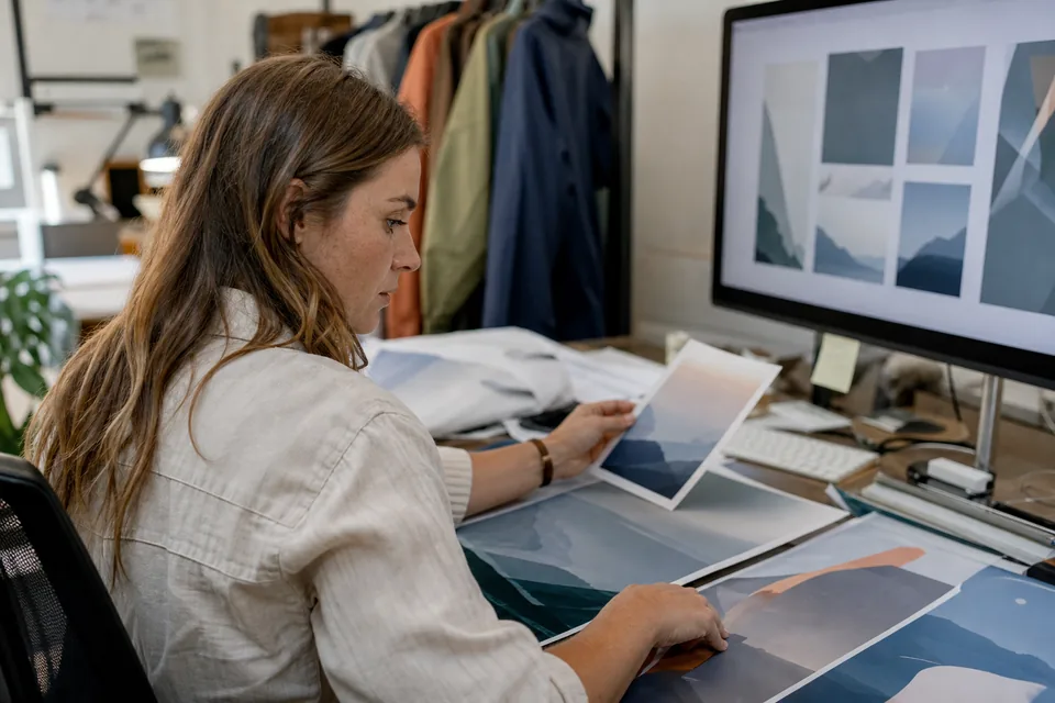 E-commerce marketer comparing banner proofs in many sizes on a large monitor and printouts