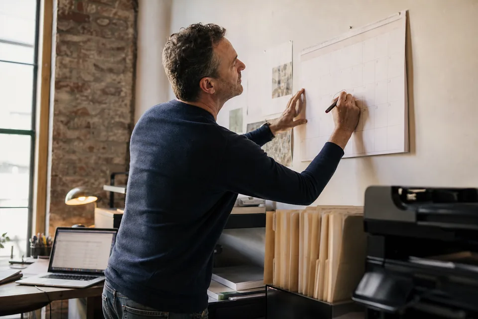 Small agency owner marking a renewal notice date on a wall calendar next to a laptop